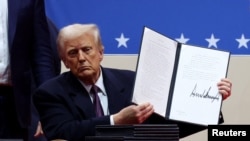 Трамп показывает подписанный им документ на сцене стадиона Capital One Arena