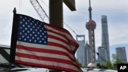 FILE - A U.S. flag flies on a U.S. Consulate car, with the backdrop of buildings in the Lujiazui financial district, in Shanghai, July 31, 2019. 