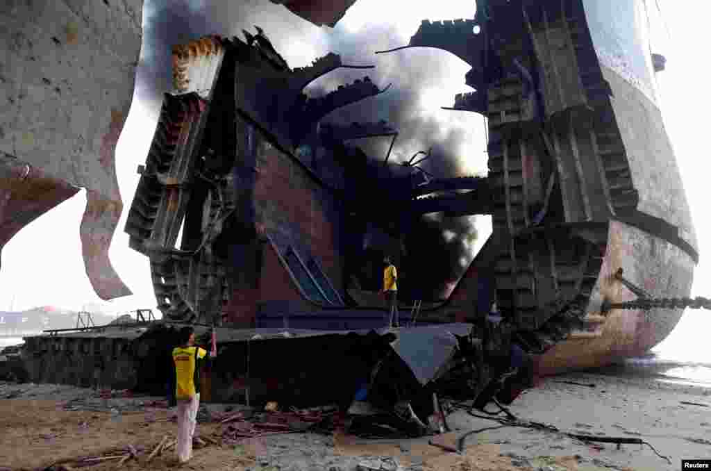 A man takes a photo of his colleague with a mobile phone on the burning oil tanker at the ship-breaking yard in Gaddani, Pakistan, Nov. 2, 2016.