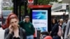 FILE - Pedestrians use their mobile phones near a Huawei advertisement at a bus stop in central London, April 29, 2019.