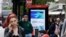FILE - Pedestrians use their mobile phones near a Huawei advertisement at a bus stop in central London, April 29, 2019.