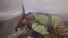 FILE - Two children and their mother rest under a mosquito net.