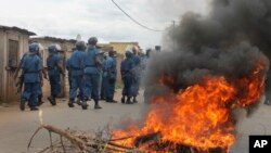 Polisi anti huru-hara Burundi melewati ban yang dibakar setelah bentrokan dengan demonstran oposisi di sebuah jalanan di ibukota Bujumbura, Burundi Minggu, 26 April 2015. Ratusan orang di Burundi berdemo setelah partai berkuasa menominasikan Presiden Pierre Nkurunziza untuk mencalonkan diri untuk masa jabatan ketiga. (AP Photo)