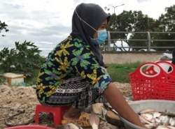 អ្នកស្រី ច្វា រីយ៉ា​ កំពុង​អង្គុយលក់​ត្រី​នៅ​ក្បែរ​ផ្លូវ​ជិត​មាត់​ទន្លេ​ក្នុង​សង្កាត់ជ្រោយ​ចង្វារ រាធានី​ភ្នំពេញ នៅ​ថ្ងៃ​ទី​២២ ខែ​ឧសភា ឆ្នាំ​២០២១។​ (កាន់ វិច្ឆិកា/វីអូអេ)