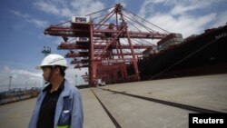 An employee stands next to a container ship at Ningbo port in Ningbo, Zhejiang province, June 21, 2012. 