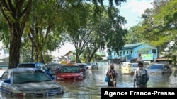 People walk past cars partially submerged in floodwaters in Shah Alam, Selangor on Dec. 21, 2021, as Malaysia faces massive floods.