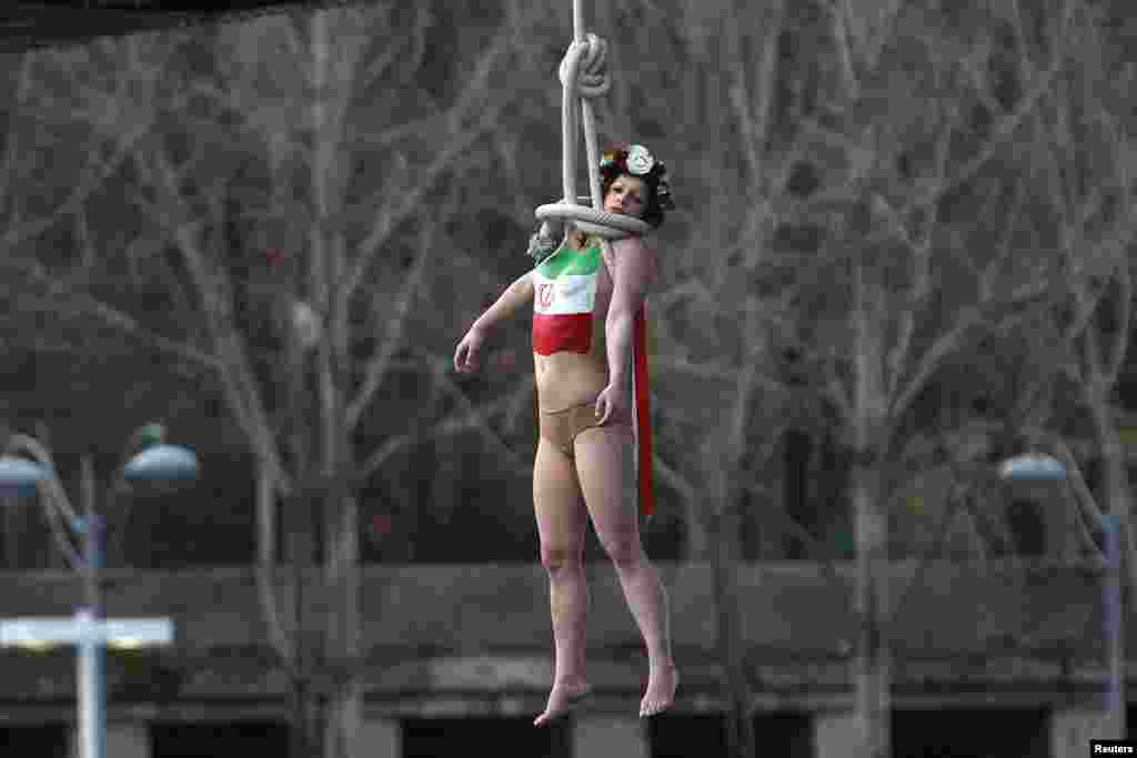 یک زن نیمه برهنه، از گروه فمن ها که معمولا اعتراض خود را با برهنگی انجام می دهند، در حالیکه پرچم جمهوری اسلامی ایران را بر روی سینه خود نقاشی کرده، به شکل نمادین خود را حلق آویز کرده است. اشاره او به آمار بالای اعدام ها در ایران است.