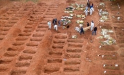 FILE - Cemetery workers in protective clothing bury three victims of the new coronavirus at the Vila Formosa cemetery in Sao Paulo, Brazil, July 15, 2020.