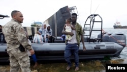 Un migrant portant un enfant, débarque d’un bateau de l’armée sous la surveillance d’un militaire de la marine libyenne à Tripoli, Libye, 7 septembre 2015