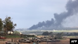 2024年1月14日，以色列和哈马斯的战争进入第100天，在以色列与加沙地带的边境地带，以色列士兵站在坦克旁边。以色列的炮击使加沙地带浓烟滚滚。（法新社）