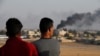 People standing on a rooftop in Akcakale, Sanliurfa province, southeastern Turkey, at the border with Syria, watch as in the background smoke billows from fires caused by Turkish bombardment in Tal Abyad, Syria, Sunday, Oct. 13, 2019.
