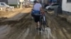A man carries his bicycle on a mud-covered street in Hiroshima, southwestern Japan, Wednesday, July 11, 2018. 