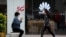 A woman wearing a face mask to help curb the spread of the coronavirus browses her smartphone as a masked woman walks by the Huawei retail shop promoting it 5G network in Beijing Oct. 11, 2020.
