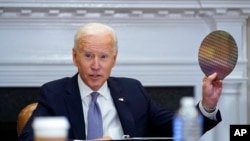 President Joe Biden holds up a silicon wafer as he participates virtually in the CEO Summit on Semiconductor and Supply Chain Resilience in the Roosevelt Room of the White House, April 12, 2021.