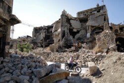 FILE - A man rides his motorcycle through the rubble of the old city of Aleppo, Syria, July 27, 2019.