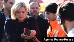 Kandidat presiden Prancis dari kubu sayap kanan Marine Le Pen (kiri) tampak memegang seekor ayam ketika berada di pekan agrikultur di Poussay, Prancis, pada 23 Oktober 2021. (Foto: AFP/Jean-Christophe Verhaegen)