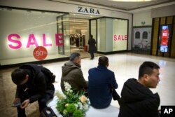 2018年1月12日，在北京一家购物中心的Zara商店外，购物者们看着他们的智能手机。