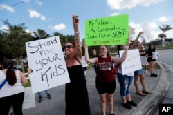 FILE - Angelina Lazo, 18, center, a senior at Marjory Stoneman Douglas High School, holds signs with other students and parents against gun violence at an intersection near the Marjory Stoneman Douglas High School in Parkland, Florida, Feb. 18, 2018.