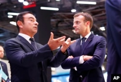 French President Emmanuel Macron listens to Carlos Ghosn, the CEO of French car maker Renault, left, at the Renault stand during an official visit at the Paris Motor Show, in Paris, France, Oct. 3, 2018.