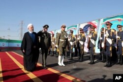 In this photo released by the official website of the office of the Iranian Presidency, President Hassan Rouhani, left, reviews an honor guard as he is accompanied by his Defense Minister Gen. Amir Hatami during a ceremony to unveil Iran-made Bavar-373 air-defense missile system, Iran, Thursday, Aug. 22, 2019. (Iranian Presidency Office via AP)
