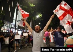 GEORGIA -- An opposition demonstrator waves Georgian national flags as he and others march on the main street near the Georgian parliament building in Tbilisi, Georgia, Monday, June 24, 2019.