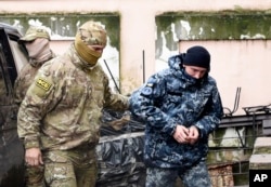 FILE - A Ukrainian sailor seized by Russia, right, is escorted by a Russian intelligence officer to a court room in Simferopol, in Russia-annexed Crimea, Nov. 27, 2018.