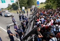 FILE - Migrants stand in front of a barrier at the border with Hungary near the village of Horgos, Serbia, Sept.15, 2015.
