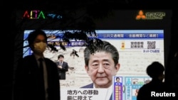 A pedestrian wearing a protective mask walks past a large screen on a building showing Japan's Prime Minister Shinzo Abe declaring a state of emergency, following the coronavirus disease (COVID-19) outbreak, in Tokyo, Japan April 7, 2020. REUTERS…