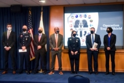 Law enforcement officials stand in front of an Operation Trojan Shield logo at a news conference, in San Diego, June 8, 2021.