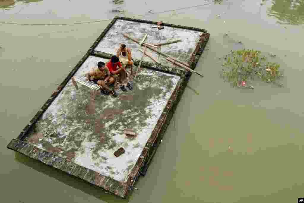 Men sit on the roof of a house which is submerged in the floodwaters of the River Ganges after heavy monsoon rains in Salori, India.