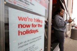 FILE - In this Nov. 27, 2019 photo a passer-by walks past a hiring for the holidays sign near an entrance to a Target store location, in Westwood, Mass.