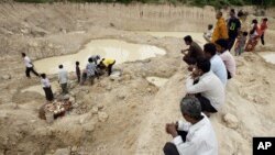 Local villagers sit and observe others preparing for a memorial service at a grave site of Phnom Trungbat in Do Dontrei village, about 60 kilometers (40 miles) northwest of Siem Reap in Cambodia, Thursday, Aug. 9, 2012. More than 100 people attended a Buddhist ceremony in rural Cambodia at the site of a freshly dug Khmer Rouge mass grave. Buddhist monks led prayers and people came with offerings of food and drinks Thursday, five days after about 20 skulls and bone fragments were unearthed at the site of a former Khmer Rouge prison. (AP Photo/Heng Sinith)