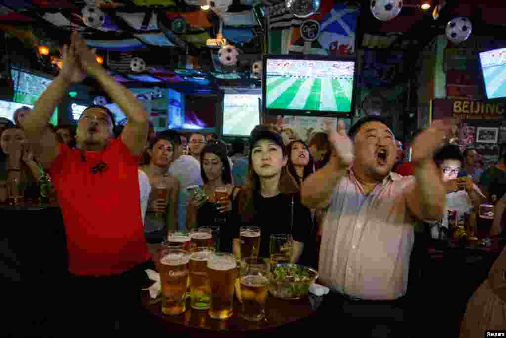 2018年6月14日，中国和外国球迷在北京的一家酒吧观看世界杯甲组俄罗斯对沙特阿拉伯足球比赛，他们看得很投入，聚精会神。
