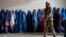 FILE - A Taliban fighter stands guard as women wait to receive food rations distributed by a humanitarian aid group, in Kabul, Afghanistan, May 23, 2023. 