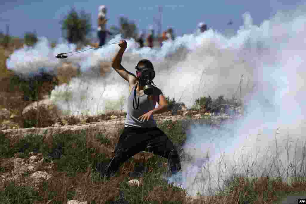 Seorang demonstran Palestina yang mengenakan masker, berusaha &quot;mengembalikan&quot; kaleng gas air mata yang ditembakkan oleh pasukan Israel pada aksi protes di desa Nabi Saleh, utara Ramallah, Tepi Barat yang diduduki Israel.