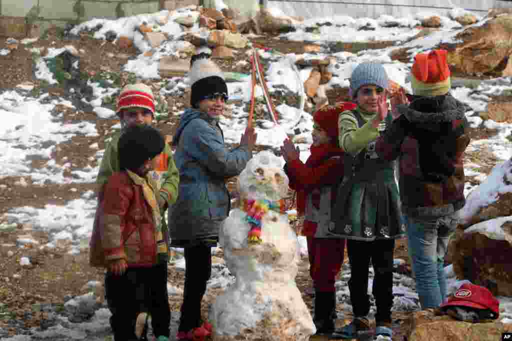 Anak-anak pengungsi Suriah bermain dekat boneka salju di kamp pengungsi Suriah di lembah Bekaa, Lebanon timur (12/12). (AP/Mohammed Zaatari)