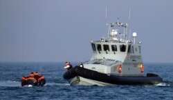 A Border Force vessel assists a group of people thought to be migrants on board from their inflatable dinghy in the English Channel, Aug. 10, 2020. The British government tries to curb the number of people crossing from France in small boats.