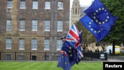An anti-Brexit protester carries flags opposite the Houses of Parliament in London, Britain, May 10, 2018. Britain's ruling party is divided over how it wants to withdraw from the European Union.
