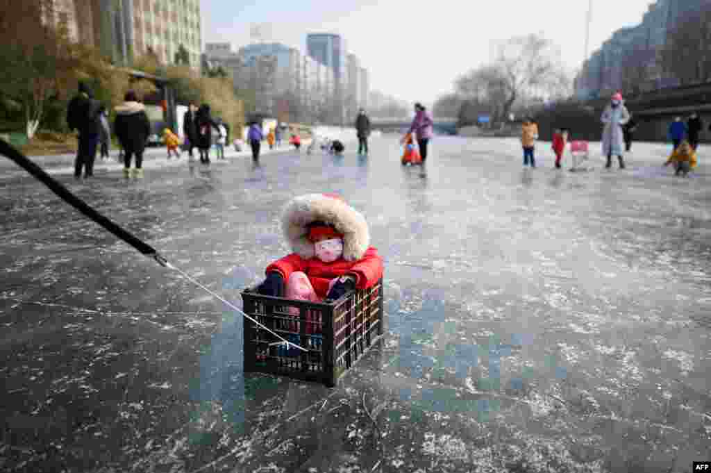 Seorang pria (tidak tampak) menarik anaknya yang duduk di dalam kotak di sungai yang membeku pada musim dingin di Beijing, China 22 Januari 2021. (Foto: Wang Zhao / AFP)