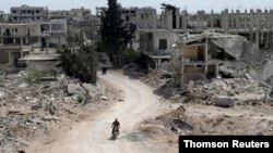 FILE - A man rides a motorbike past damaged buildings in the rebel-held town of Nairab, Idlib region, Syria, April 17, 2020. 