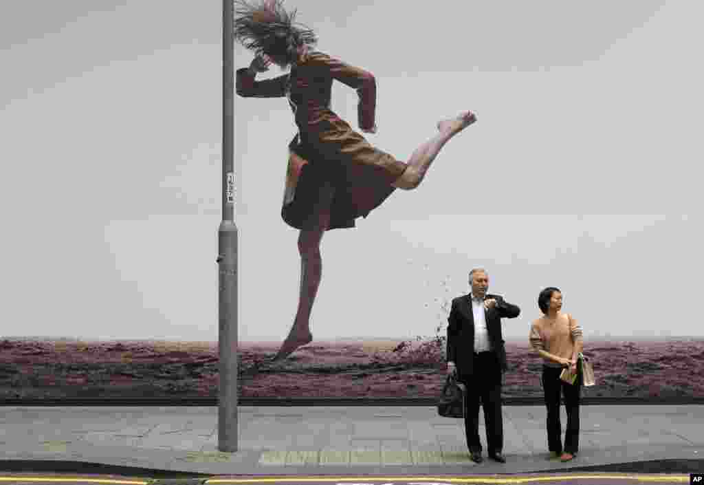 បុរស​ និង​ស្រ្តី​ម្នាក់​ឈរ​ពី​មុខ​ការ​ផ្សាយពាណិជ្ជកម្ម​ពី​ការ​បង្ហាញ​ម៉ូដ​តាម​បណ្តោយ​ផ្លូវ​នៅ​ក្រុង​ហុងកុង។