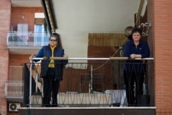 A caregiver (R) keeps her distance from an elderly woman whom she looks after, on the balcony of the woman's home in Rome, March 11, 2020.