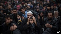 이라크 정부 군과 ISIL 간 교전을 피해 집을 떠난 모술 주민들이 난민캠프로 이동하기 위해 검문소에서 줄을 서 있다. 한 남성이 총격 소리가 들리자 아들의 귀를 막고 있다. 