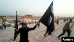 FILE - A fighter of the Islamic State of Iraq and the Levant (ISIL) holds an ISIL flag and a weapon on a street in the city of Mosul, June 23, 2014.