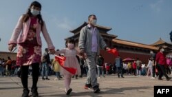 A family wearing face masks as a preventive measure against the Covid-19 coronavirus walk outside the Forbidden City (back) during the national day marking the 71st anniversary of the People's Republic of China and the country's national "Golden Week" hol