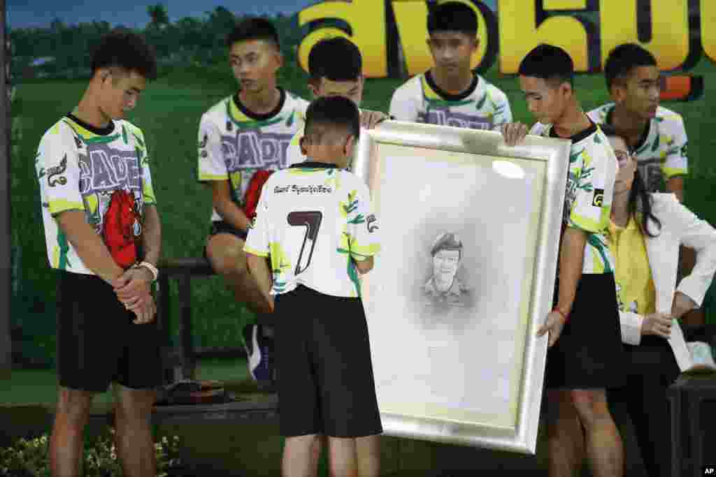 Coach Ekkapol Janthawong, left, and the 12 boys on the Thai soccer team that had been trapped in the cave pay their respects and thanks as they hold a portrait of Saman Gunan, the retired Thai SEAL diver who died during their initial rescue attempt, during a press conference in Chiang Rai, northern Thailand.
