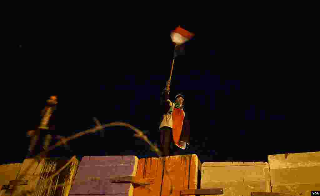 An anti-Morsi protester waves an Egyptian flag atop a huge wall erected by Egypt's Republican Guard to prevent demonstrators from amassing around the Presidential Palace. (Yuli Weeks for VOA)