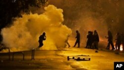 Protesters try to avoid the effects of tear gas fired by riot police during clashes in Athens, Nov. 17, 2017.