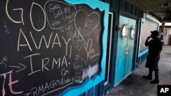 在一间已经关闭的餐馆门口的黑板上，写着希望飓风离开的文字。