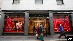 FILE - People walk in front of Gucci shop in Monte Napoleone street in Milan, Italy, Oct. 20, 2016. Nigerian women who were trafficked to Italy to work as prostitutes have found new work in a handbag and dressmaking shop that recently received fabric leftovers from Gucci.